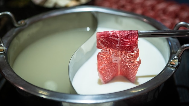 La viande crue de boeuf tient avec des baguettes. Hot pot avec un pot en laiton en Chine. Plat chinois de viande et de légumes émincés bouillis dans une soupe miso