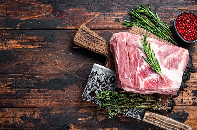 Viande crue de cou de porc pour des steaks hachés frais sur une planche à découper en bois avec un couperet de boucher. Fond en bois sombre. Vue de dessus. Espace de copie.