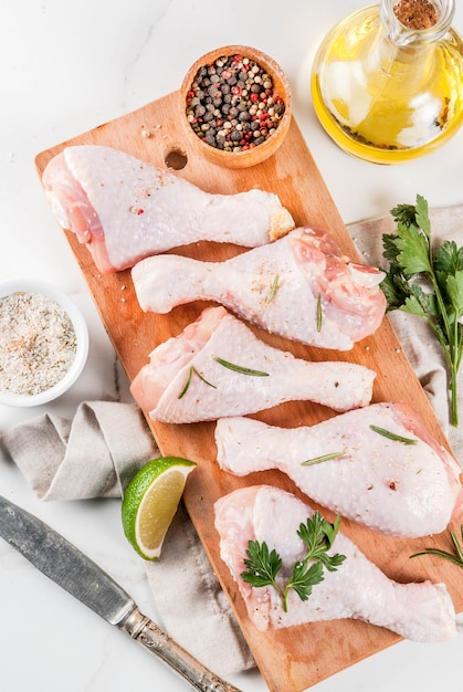 Viande crue, cuisses de poulet, avec de l'huile d'olive, des herbes et des épices, sur fond de marbre blanc, copie vue de dessus de l'espace