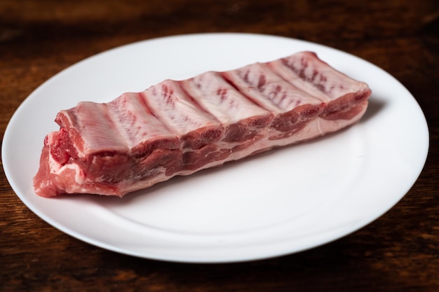 Viande crue fraîche et côtes de porc d'un plat blanc sur un fond en bois