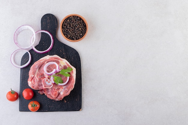 Viande crue fraîche avec des légumes et des grains de poivre placés sur une table en pierre.