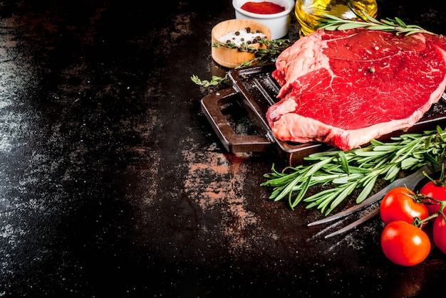 Viande crue fraîche, steak de marbre de boeuf d'agneau sur une plaque de cuisson au grill, avec des ingrédients pour la cuisson. Sur table en métal rouillé foncé, fond