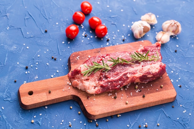 Viande crue. Un gros morceau de côtelette de boeuf sur une planche à découper en bois avec du romarin et des épices.