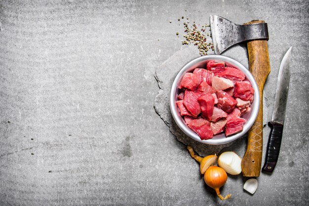 Photo viande crue hachée avec une hache, un couteau et des épices. sur la table en pierre. espace libre pour le texte. vue de dessus