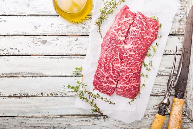 Viande crue marbrée fraîche Steak de boeuf et assaisonnements sur papier sur surface en bois blanc
