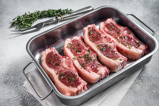 Viande crue marinée de selle de mouton d'agneau dans un plateau en acier avec des épices de thym et de l'huile d'olive Fond blanc Vue de dessus