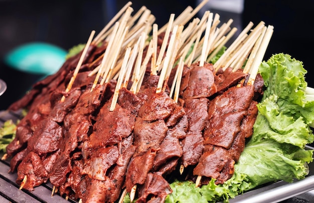 Viande crue de nourriture de rue sur des bâtons avec des feuilles de salade