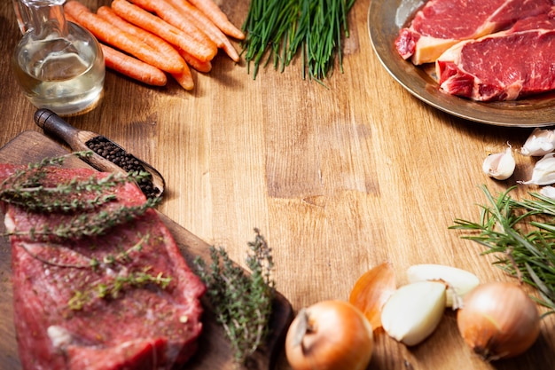 Viande crue sur planche à découper en bois et assiette vintage avec crudités placées dans un cercle avec un espace vide au milieu. Saveur d'ail. Herbes vertes.