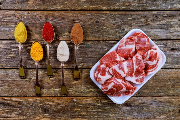 Viande crue de porc et cuillères d'ingrédients avec différentes épices sur une vieille table en bois