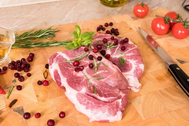 Viande crue. Steaks de porc sur une planche de bois avec des épices, des baies, de l'huile et des tomates cerises prêts à griller et barbecue