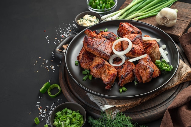 Viande délicieuse et frite avec des oignons sur fond noir avec des herbes, des sauces et des épices. Vue latérale, espace pour la copie.