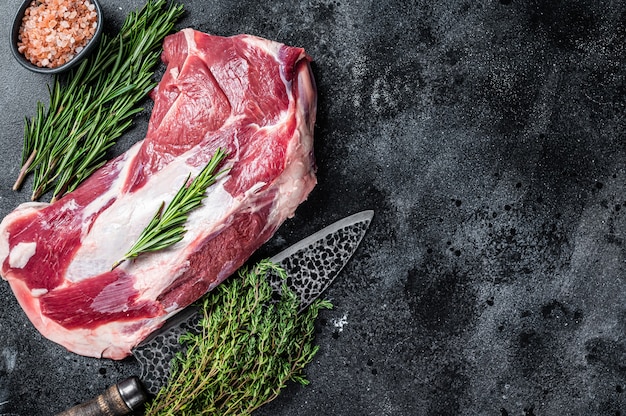 Viande d'épaule de mouton d'agneau cru frais avec couteau de boucher. Fond noir. Vue de dessus. Espace de copie.