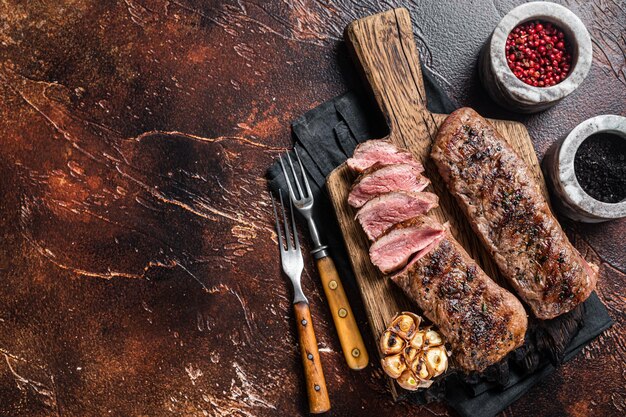 Viande de filet de surlonge d'agneau grillé sur planche de bois aux herbes, steak de longe de mouton. Fond sombre. Vue de dessus. Espace de copie.