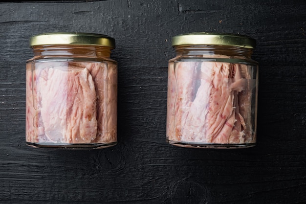 Photo viande de filet de thon dans un bocal en verre sur table en bois noir, mise à plat