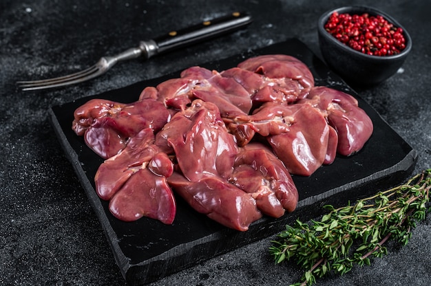 Viande de foie de poulet cru sur planche de marbre avec du thym. Table noire. Vue de dessus.