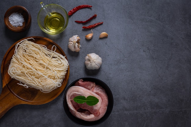 Viande fraîche, boeuf ou porc sur un bloc de bois à découper avec des ingrédients pour la cuisson sur une table en ciment foncé