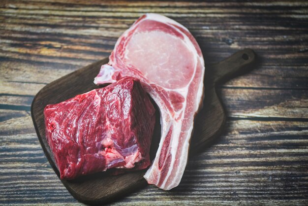 Viande fraîche de boeuf tranché et côtelettes de porc sur fond de planche à découper en bois - Steak de boeuf cru