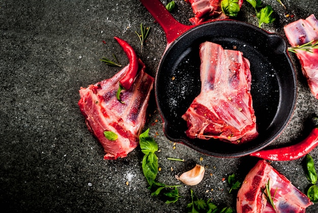 Viande fraîche crue, côtes d'agneau ou de boeuf crues avec piment, ail et épices avec poêle à frire sur pierre noire, vue de dessus