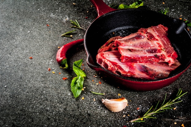 Viande fraîche crue, côtes d'agneau ou de boeuf non cuites avec du piment, de l'ail et des épices dans une poêle à frire sur fond de pierre sombre, espace copie