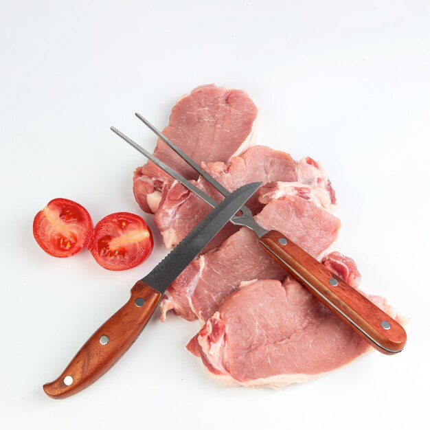Viande fraîche pour griller sur fond blanc avec couteau et fourchette à tomates