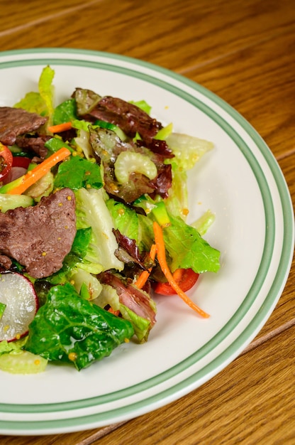 Viande frite aux légumes. Salade de viande, tomates, poivrons, concombres et salade sur fond de bois