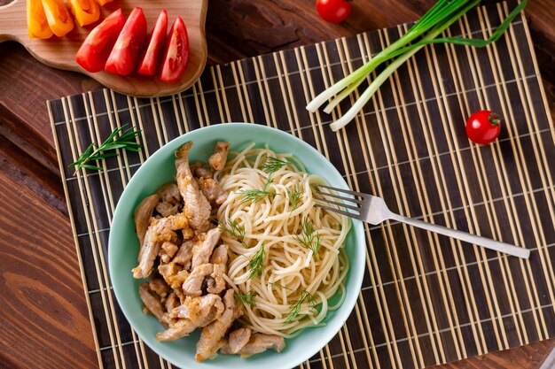 Viande frite et spaghetti sur une assiette sur un fond en bois avec des tomates et des herbes.