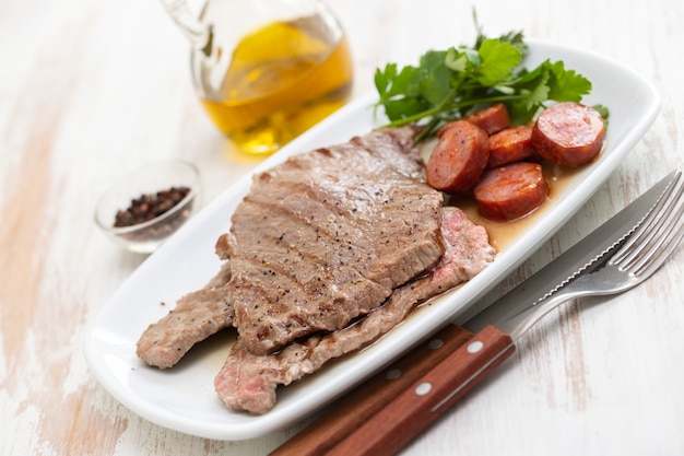 Viande grillée avec saucisse fumée sur plat blanc