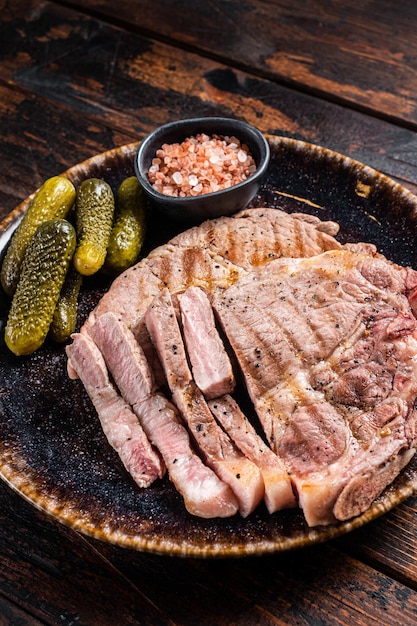 Viande grillée - Steaks de porc de viande de filet de cou dans une assiette avec des concombres marinés. Fond en bois. Vue de dessus.