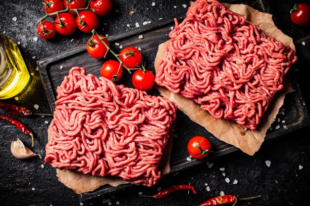 Viande hachée crue sur une planche à découper avec tomates cerises