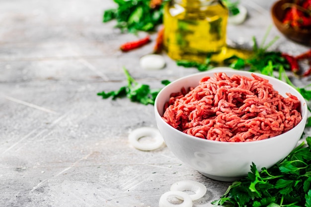 Viande hachée dans un bol sur une table avec du persil et des rondelles d'oignon