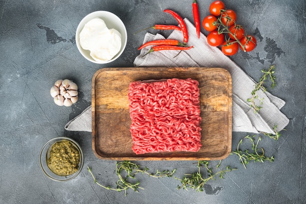 Viande hachée maison dans un bol noir avec des ingrédients. Haché cru frais pour la cuisson des boulettes de viande, sur une table en pierre grise, vue de dessus à plat