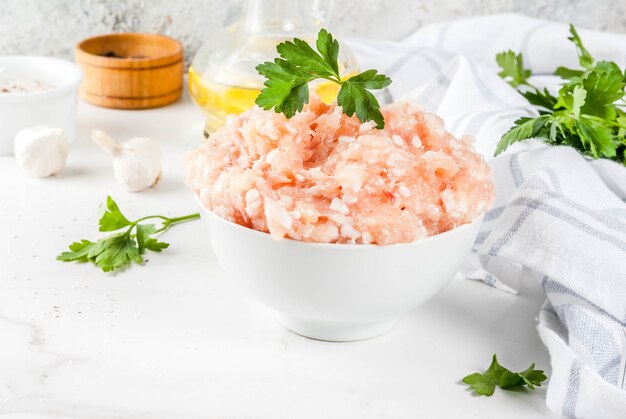 Viande hachée de poulet ou de dinde crue dans un bol blanc, avec huile, épices et fines herbes