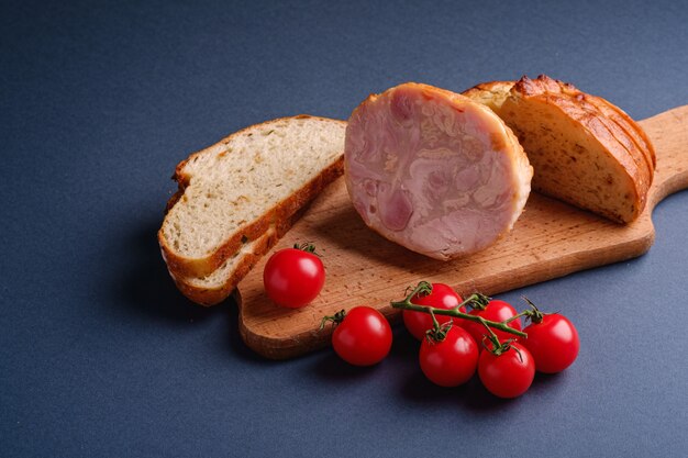 Viande de jambon de dinde, branche de tomates cerises fraîches et pain en tranches sur une planche à découper en bois, mur minimal bleu, angle de vue, espace copie