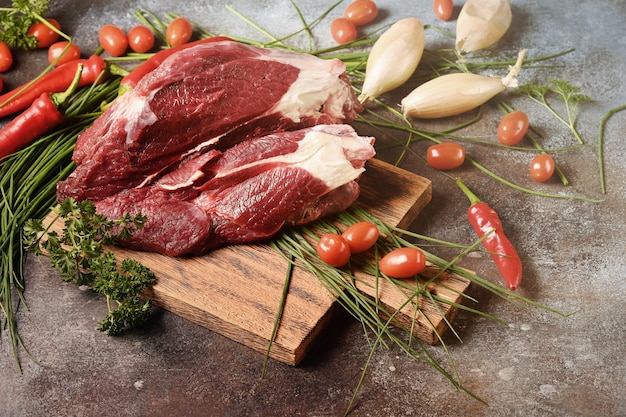 Viande noire fraîche avec des ingrédients pour la cuisson sur une planche à découper en bois brun.