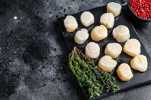 Viande de pétoncles frais de fruits de mer sur une planche de marbre. Fond noir. Vue de dessus. Espace de copie.