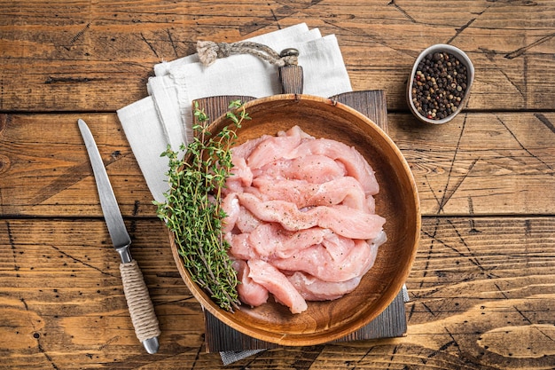 Viande de poitrine de dinde de poulet crue en tranches dans une assiette en bois avec du thym Fond en bois Vue de dessus