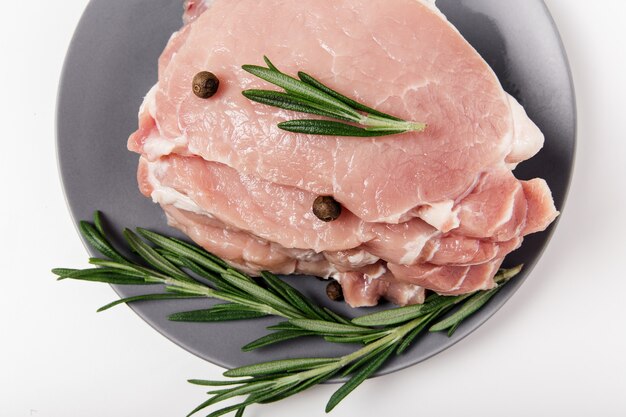 Viande de porc crue sur l'assiette avec romarin, sel et poivre.