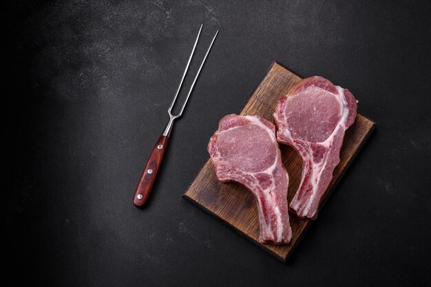 Viande de porc crue fraîche sur les côtes avec des épices et des herbes sur une planche à découper en bois sur un fond de béton foncé