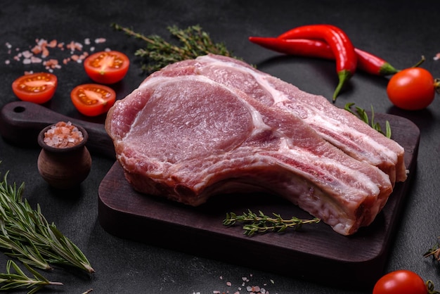 Viande de porc crue fraîche sur les côtes avec des épices et des herbes sur une planche à découper en bois sur un fond de béton foncé