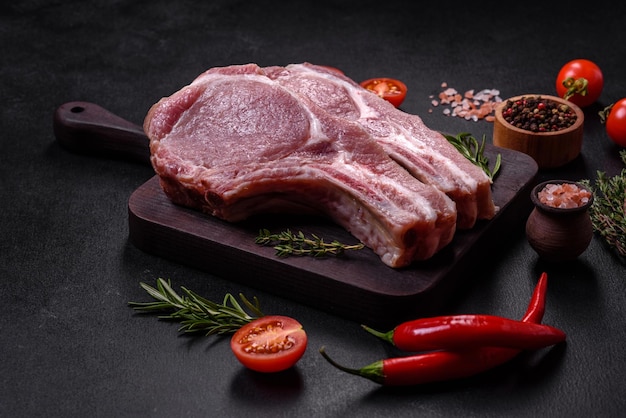 Viande de porc crue fraîche sur les côtes avec des épices et des herbes sur une planche à découper en bois sur un fond de béton foncé