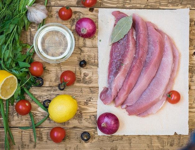 Viande de porc crue avec des herbes et des épices sur une table en bois.