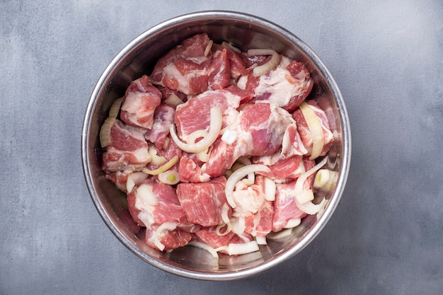 Viande de porc crue avec oignon, sel et poivre dans un bol. Viande marinée.