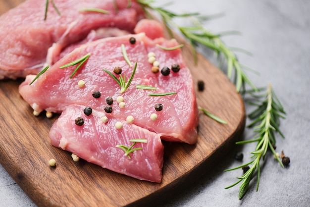 Viande de porc crue sur une planche à découper en bois sur la table de la cuisine pour la cuisson du steak de porc rôti ou grillé avec des ingrédients aux herbes et aux épices Porc frais