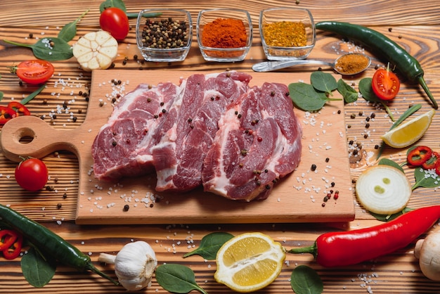 Viande de porc crue sur une planche à découper en bois à table de cuisine pour la cuisson du steak de porc rôti ou grillé avec des ingrédients herbes et épices, porc frais