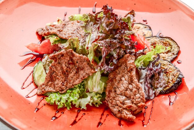 Viande de porc grillée avec salade de légumes frais sur une plaque blanche.