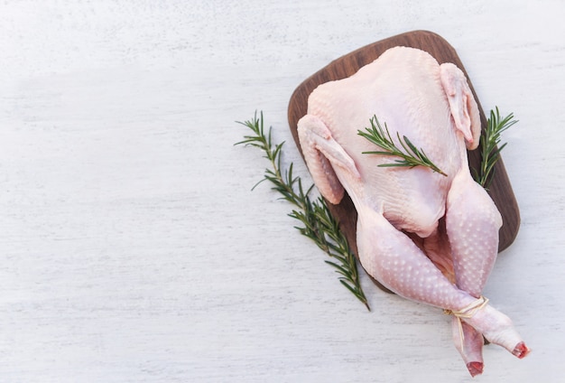 Viande de poulet au romarin / poulet cru frais entier sur planche de bois sur fond de bois blanc