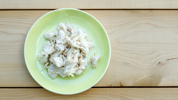 Viande de poulet bouillie dans une assiette jaune sur fond en bois.