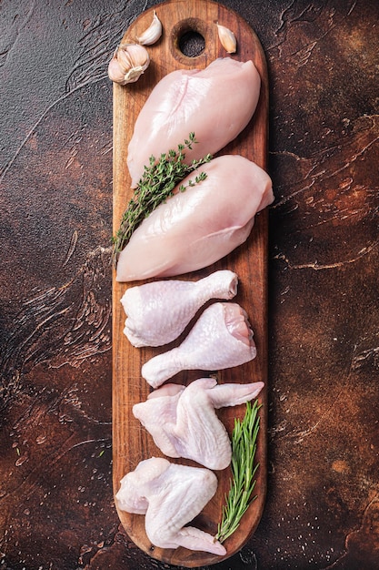 Photo viande de poulet crue assortiment de pièces pilon poitrine filet ailes cuisse aux épices fond sombre vue de dessus