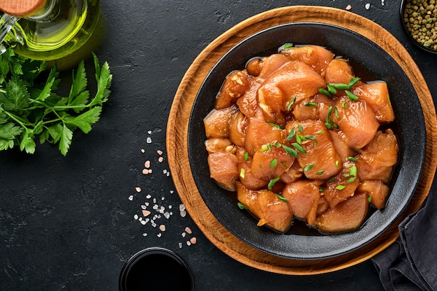 Viande de poulet crue marinée dans une sauce soja teriyaki, des oignons et du poivre dans une assiette noire sur fond d'ardoise foncée, de pierre ou de béton. Vue de dessus avec espace de copie.