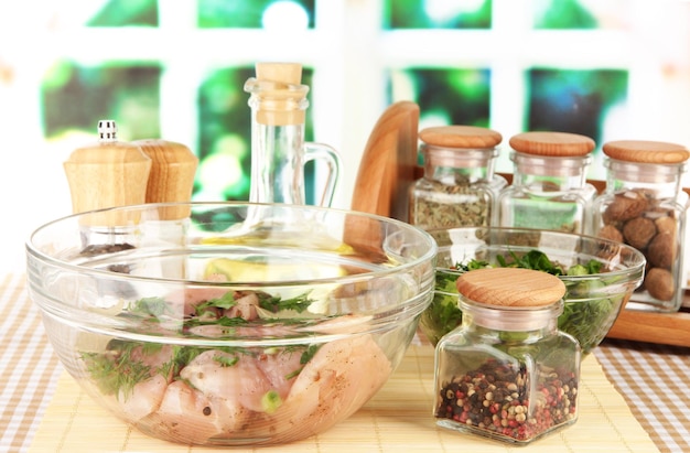 Viande de poulet dans un bol en verre herbes et épices sur table sur fond de fenêtre